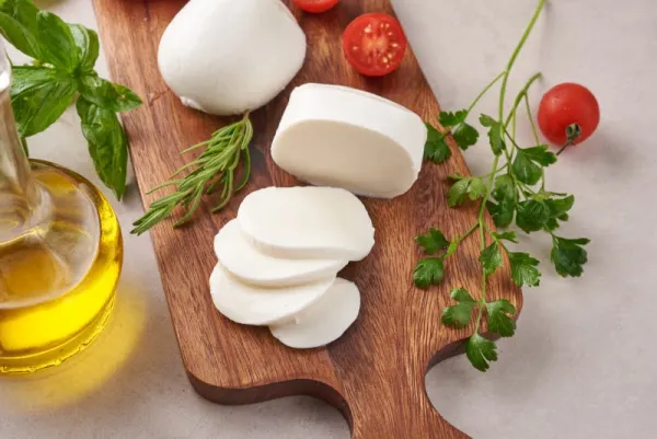  Čerstvá mozzarella nakrájaná na drevenom podnose s paradajkami, bylinkami a olivovým olejom